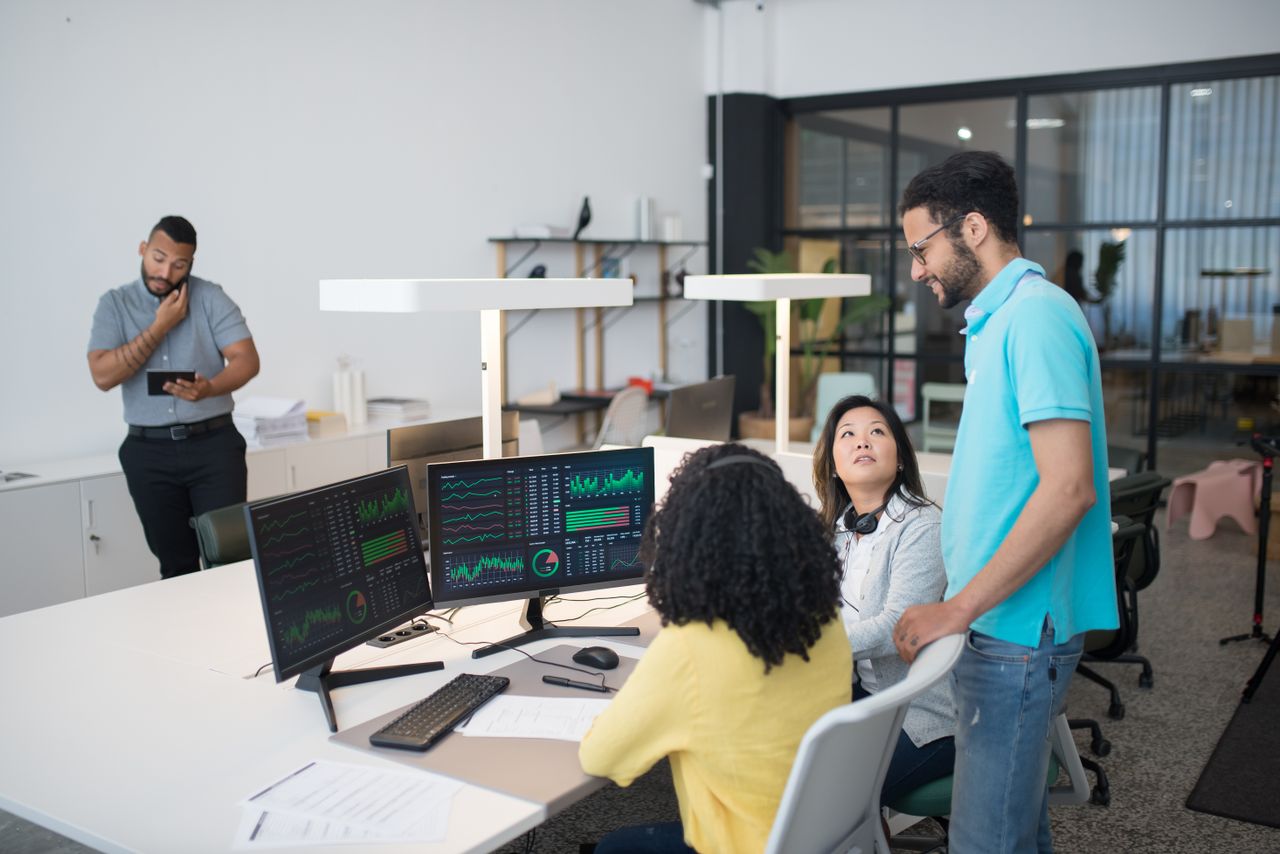 Office employees collaborate on financial data at modern workspace, engaging in teamwork and communication.